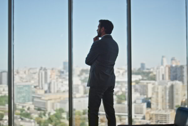Thoughtful man looking panoramic window in office. Legal manager contemplating city buildings planning company strategy at workplace rear view. Unrecognized silhouette making business decision.