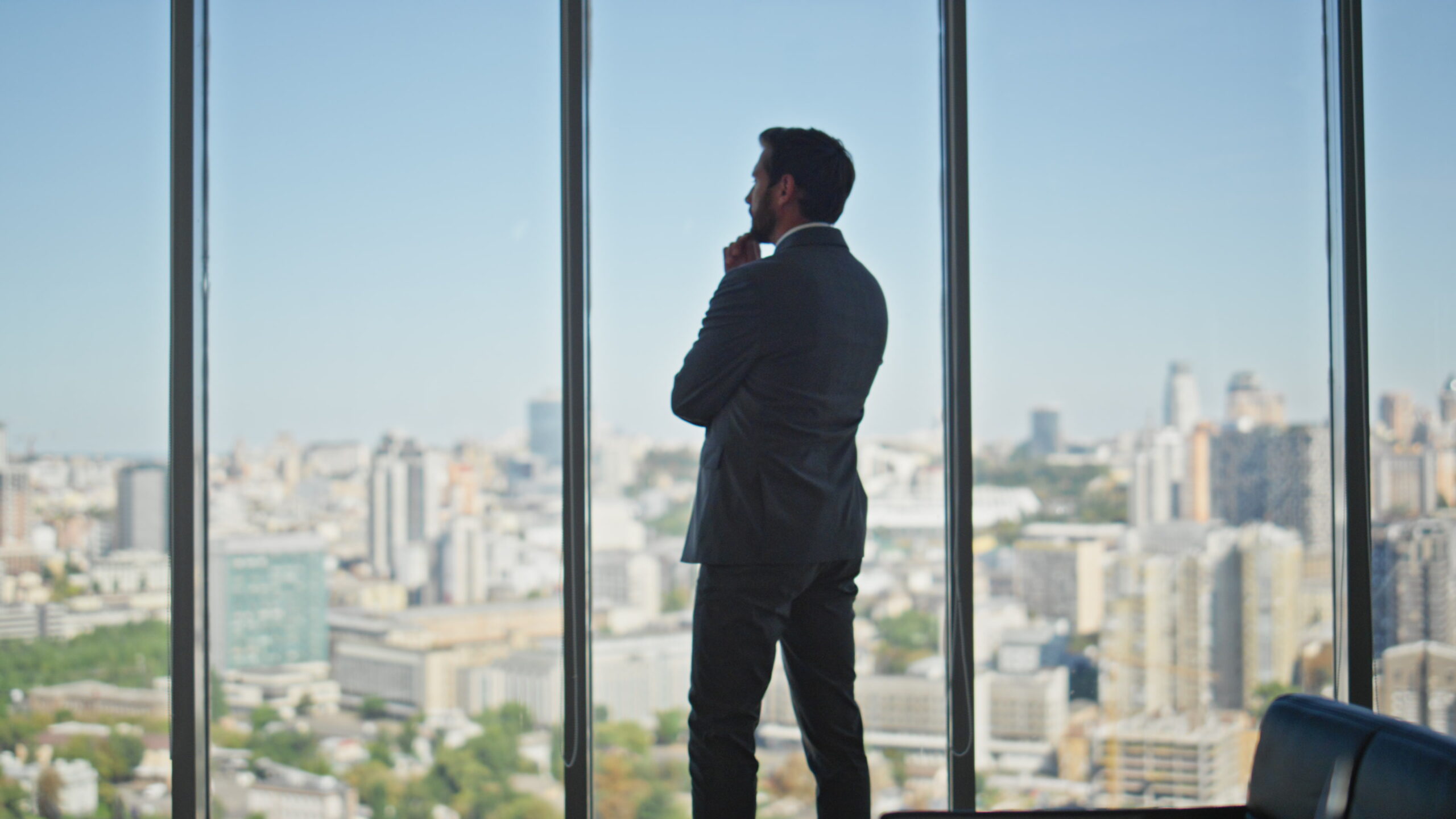 Thoughtful man looking panoramic window in office. Legal manager contemplating city buildings planning company strategy at workplace rear view. Unrecognized silhouette making business decision.